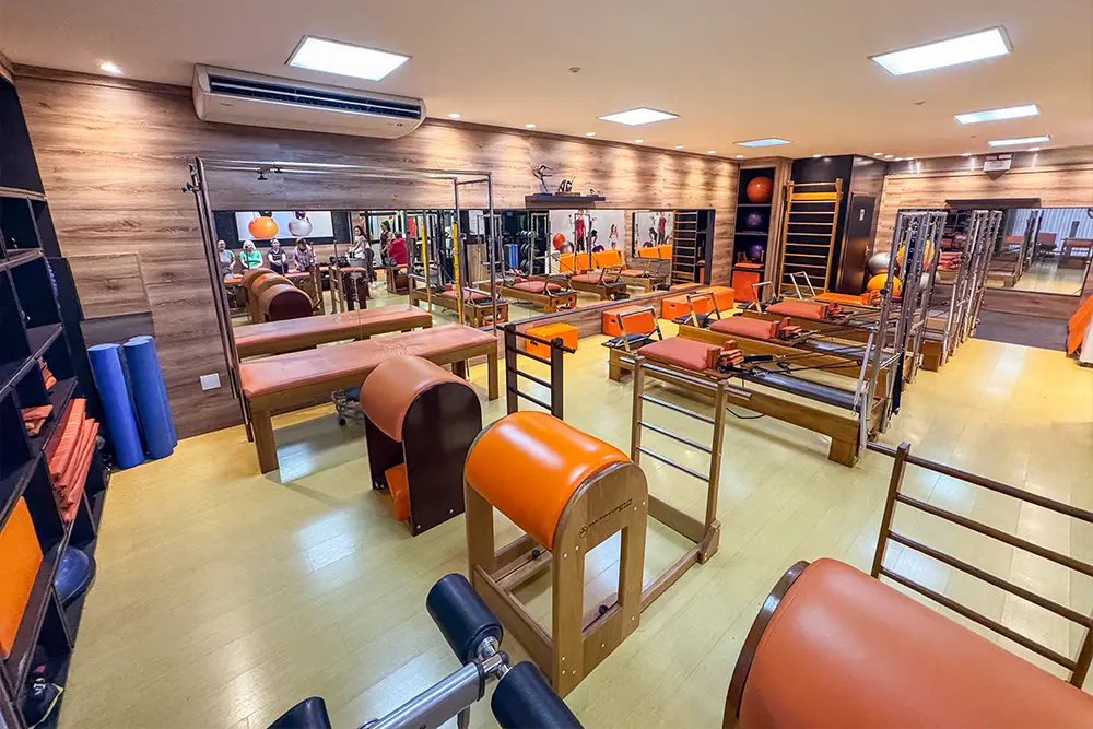 Vista ampla do estúdio de Pilates da Clínica da Coluna, com reformers, cadeiras e barris
